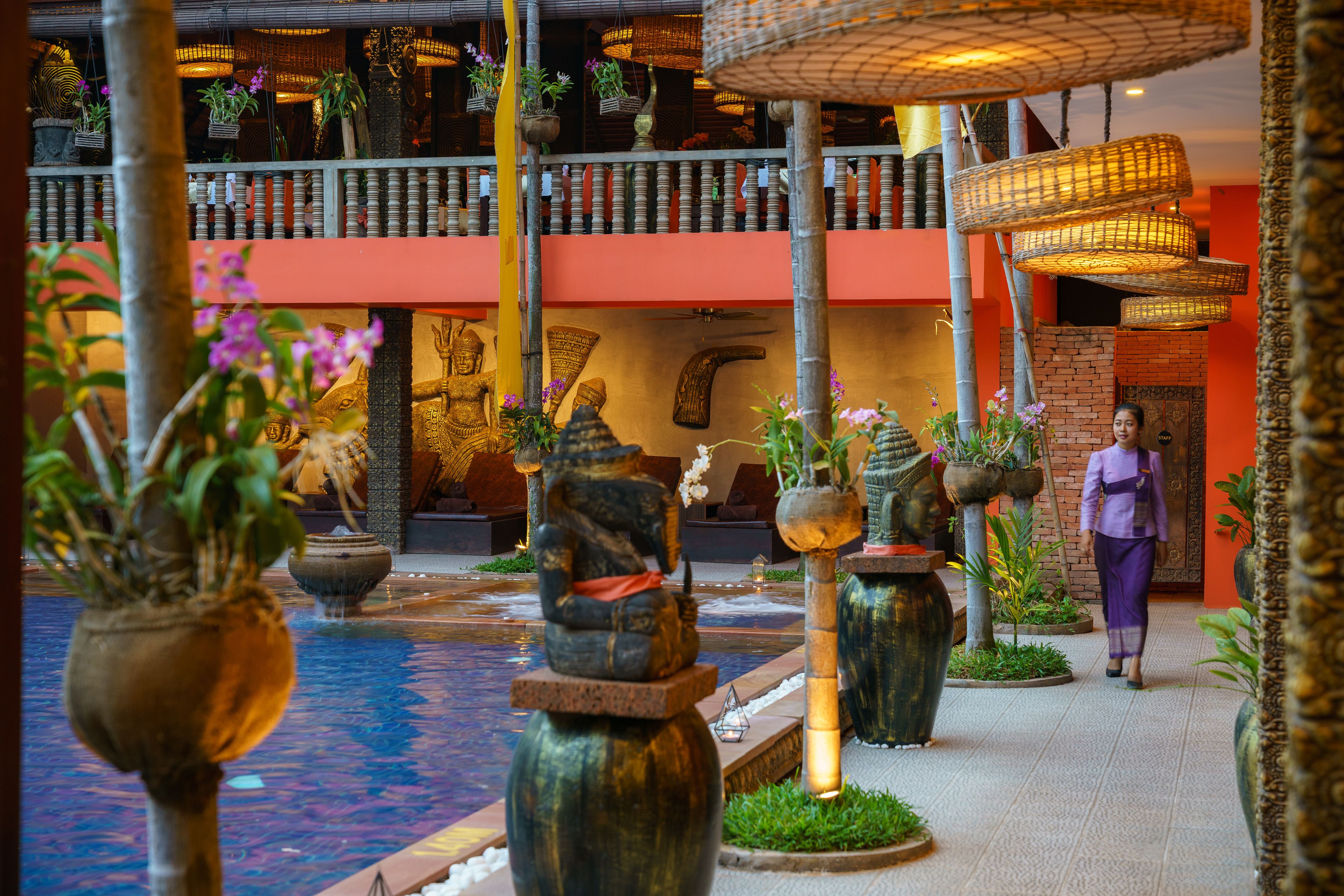 A traditional Balinese courtyard with a central water feature, stone statues, and hanging baskets with flowers.