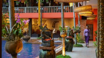A traditional Balinese courtyard with a central water feature, stone statues, and hanging baskets with flowers.
