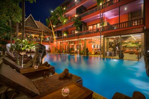 A hotel with a large outdoor pool, multiple balconies, and tropical decor.