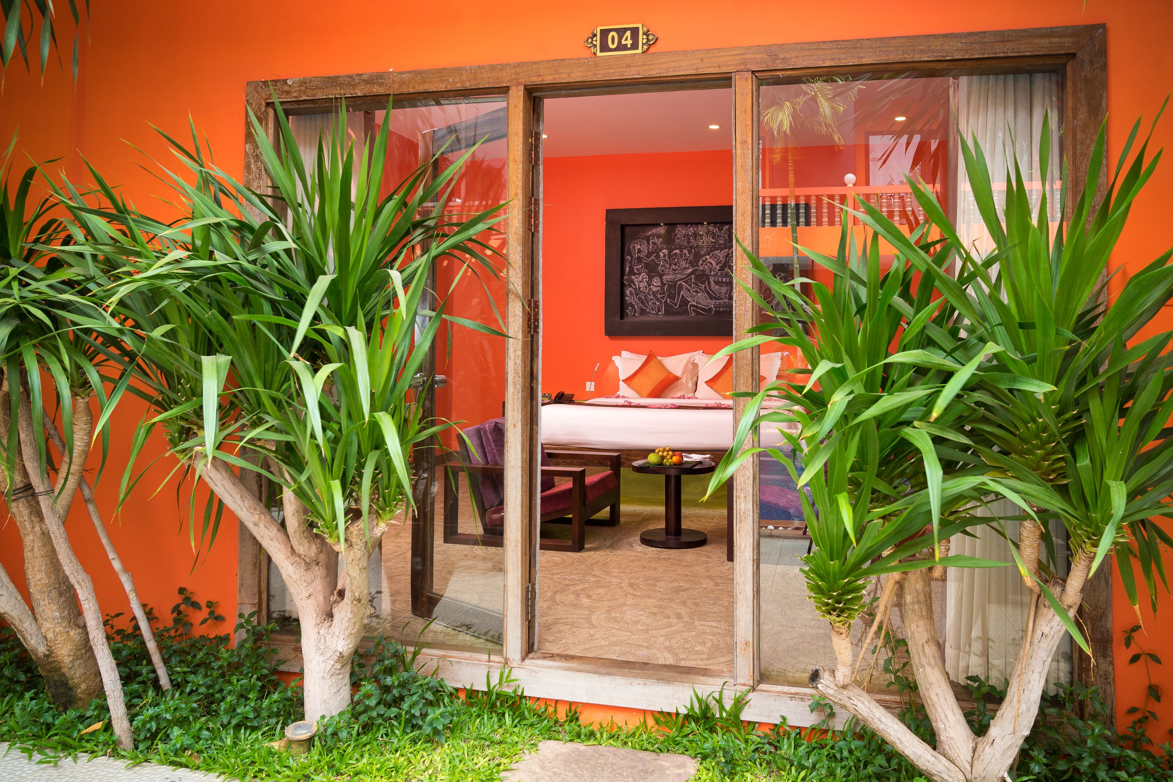 A room with a bed, a table, and chairs, surrounded by plants.