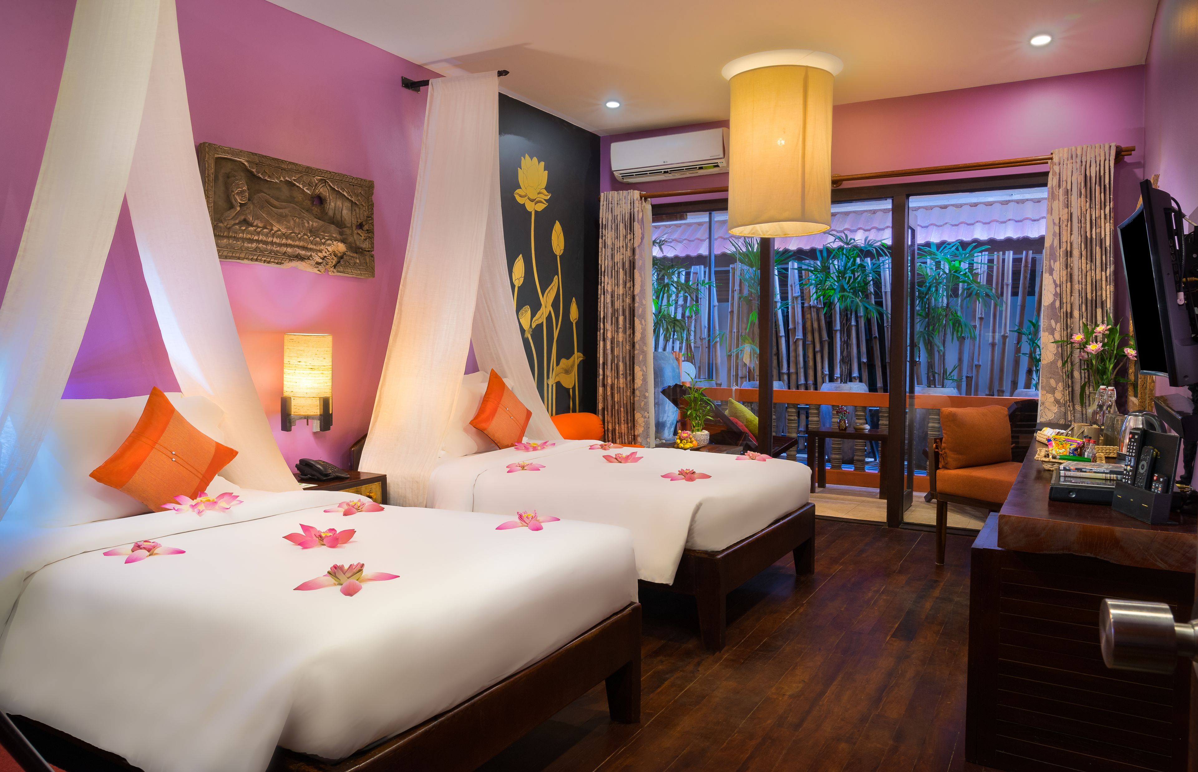 Quarto de hotel com duas camas, uma escrivaninha, uma cadeira e vista para o exterior.