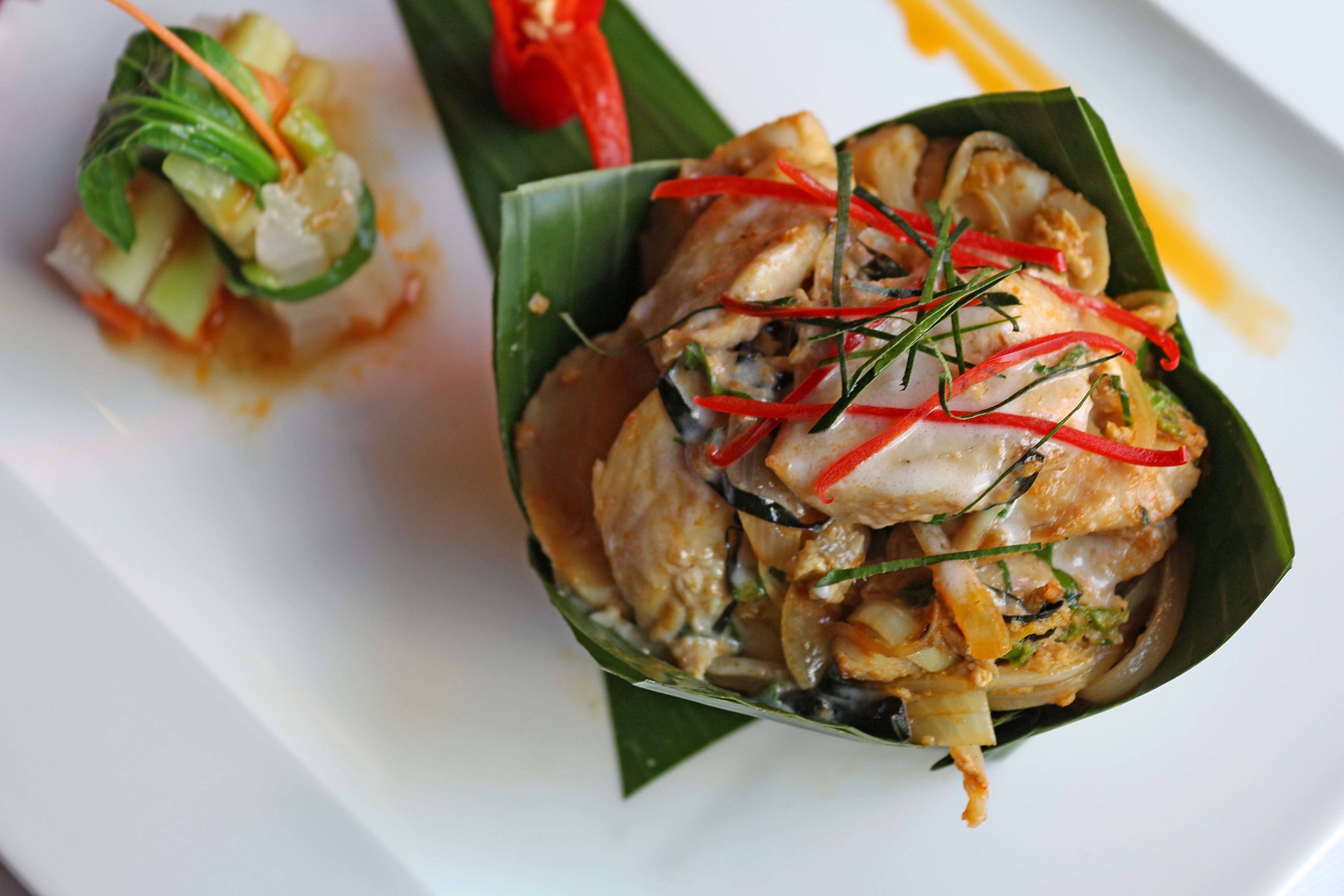 A dish of food served on a leaf, garnished with red chili and herbs.