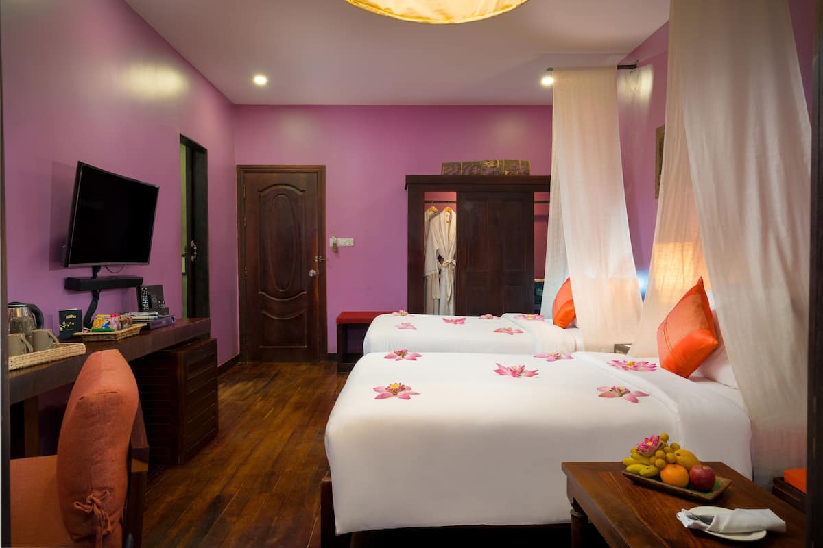 A hotel room with two beds, a desk, a TV, and a fruit basket.