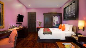 Habitación de hotel con cama, escritorio, silla, televisor, un cuadro y una cesta de frutas.