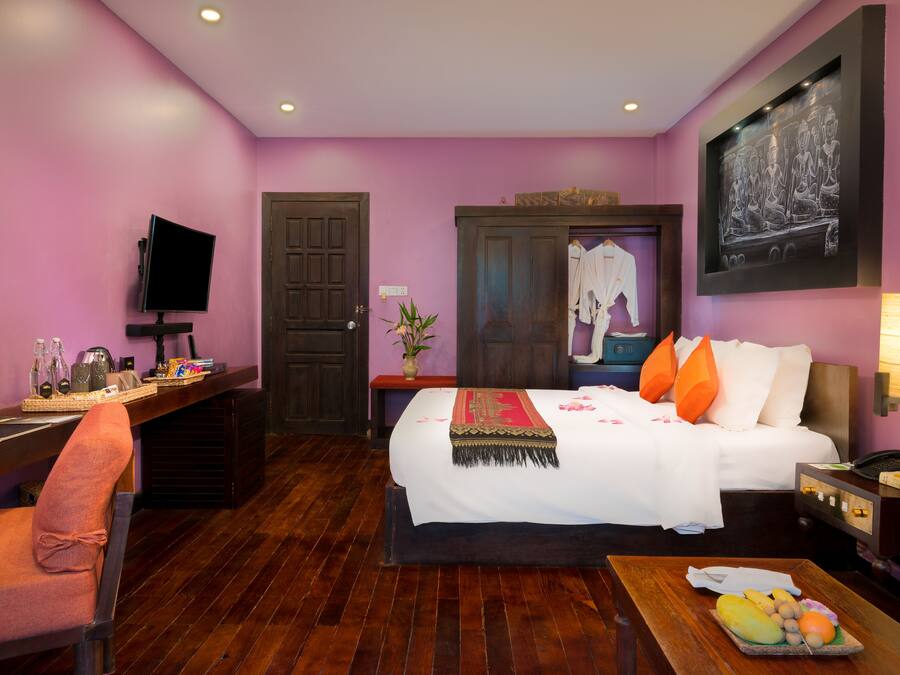 Habitación de hotel con cama, escritorio, silla, televisor, un cuadro y una cesta de frutas.