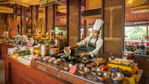 A buffet area with a variety of dishes and cooking utensils, a chef preparing food, and a sign indicating cooking classes.
