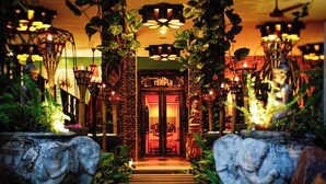 A hotel entrance with a traditional archway, illuminated by hanging lights and surrounded by lush greenery.