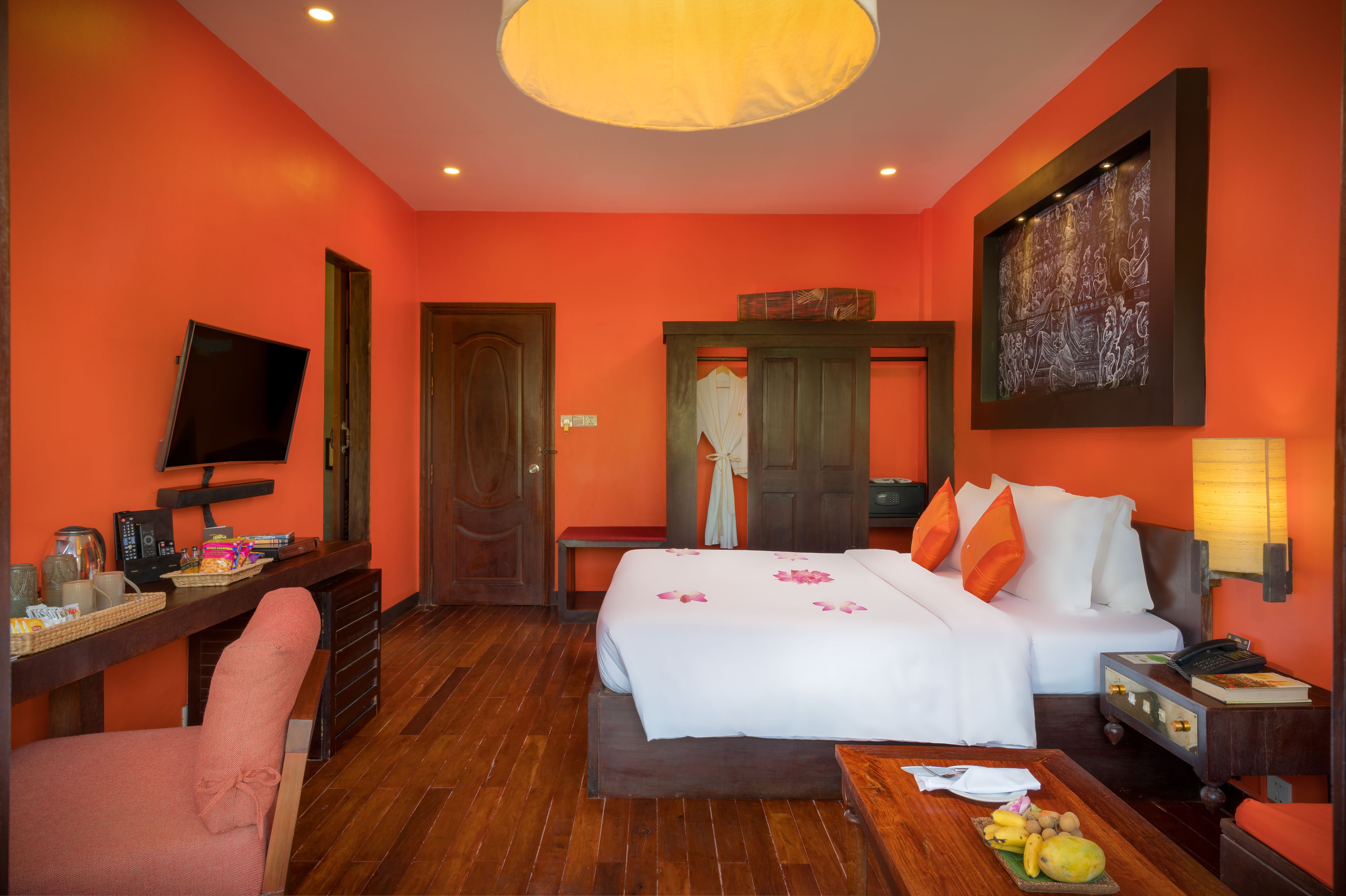 Una habitación de hotel con una cama, un escritorio con una computadora, una silla, un televisor y una cesta de frutas.