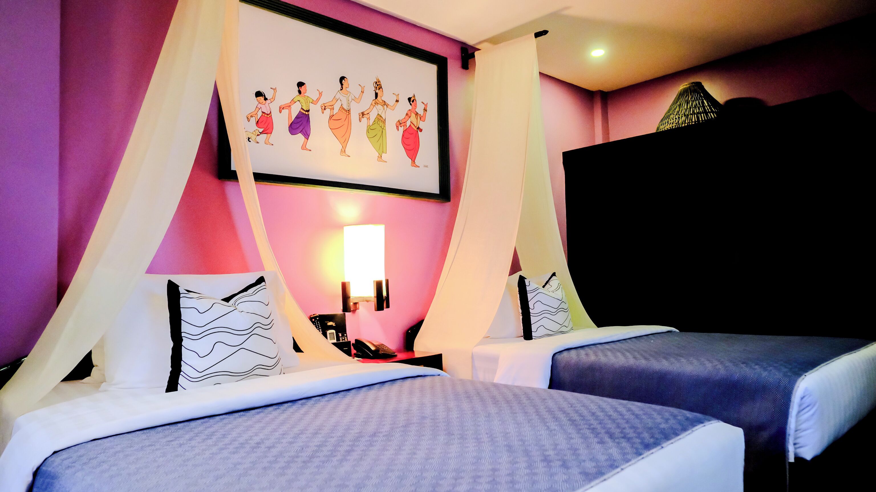 Habitació d'hotel amb dos llits, un televisor penjat a la paret, una taula de nit amb una làmpada i un adorn mural decoratiu.