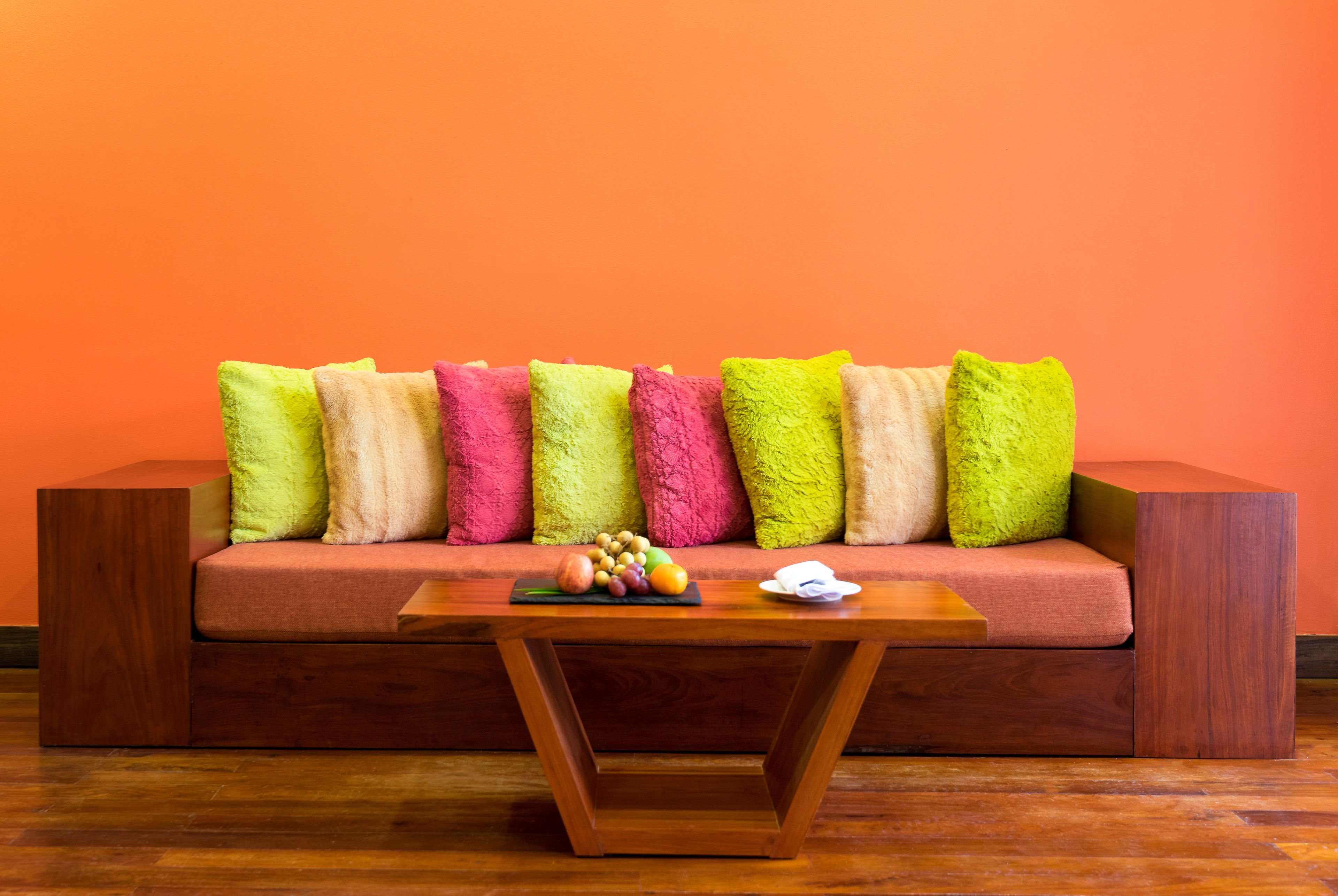 Ein modernes Wohnzimmer mit einem Holztisch, einer Couch mit bunten Kissen und einer Obstschale auf dem Tisch.