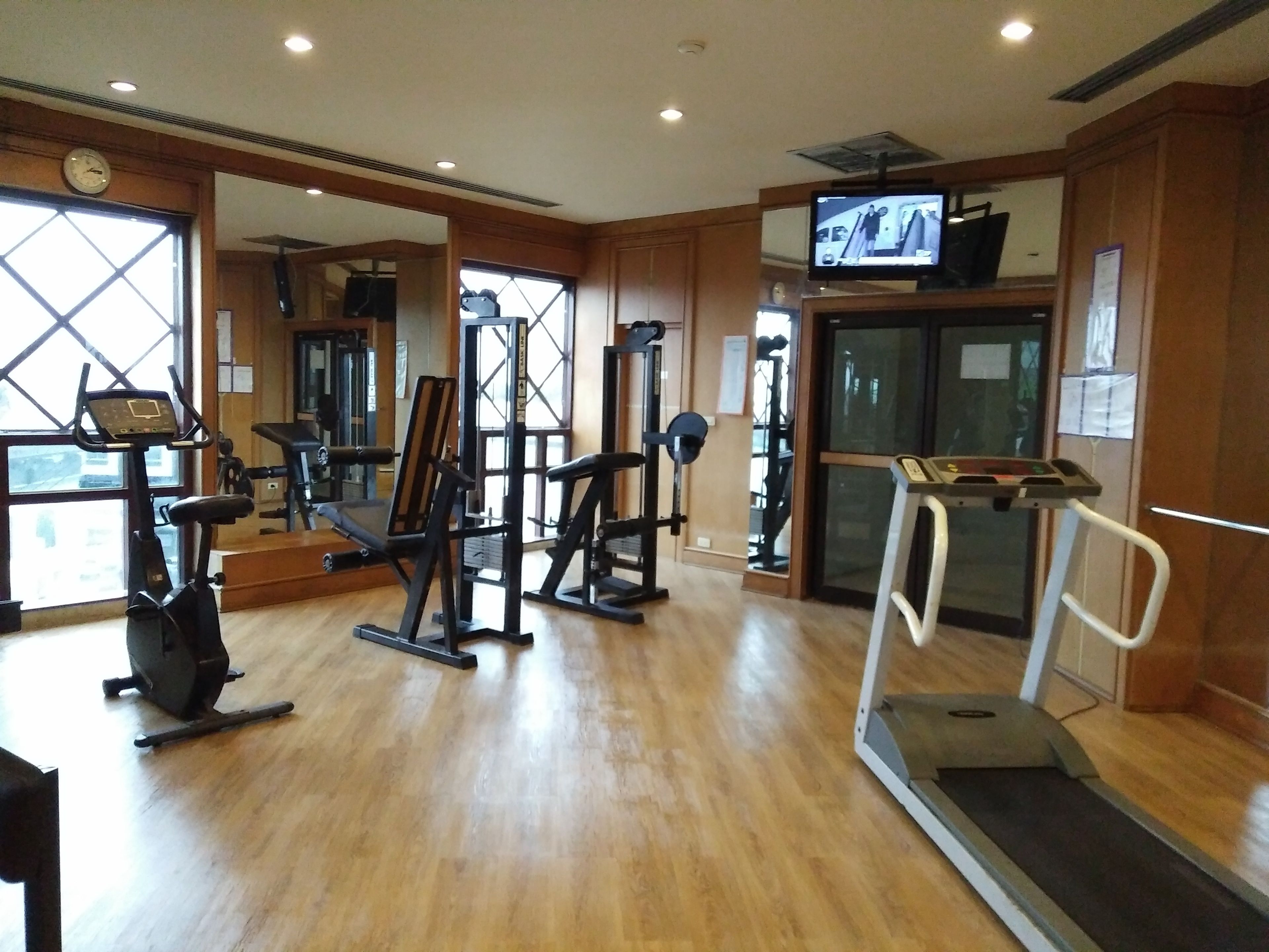 Uma academia com diversos equipamentos de exercício, incluindo esteiras, aparelhos de musculação e uma televisão fixada na parede.