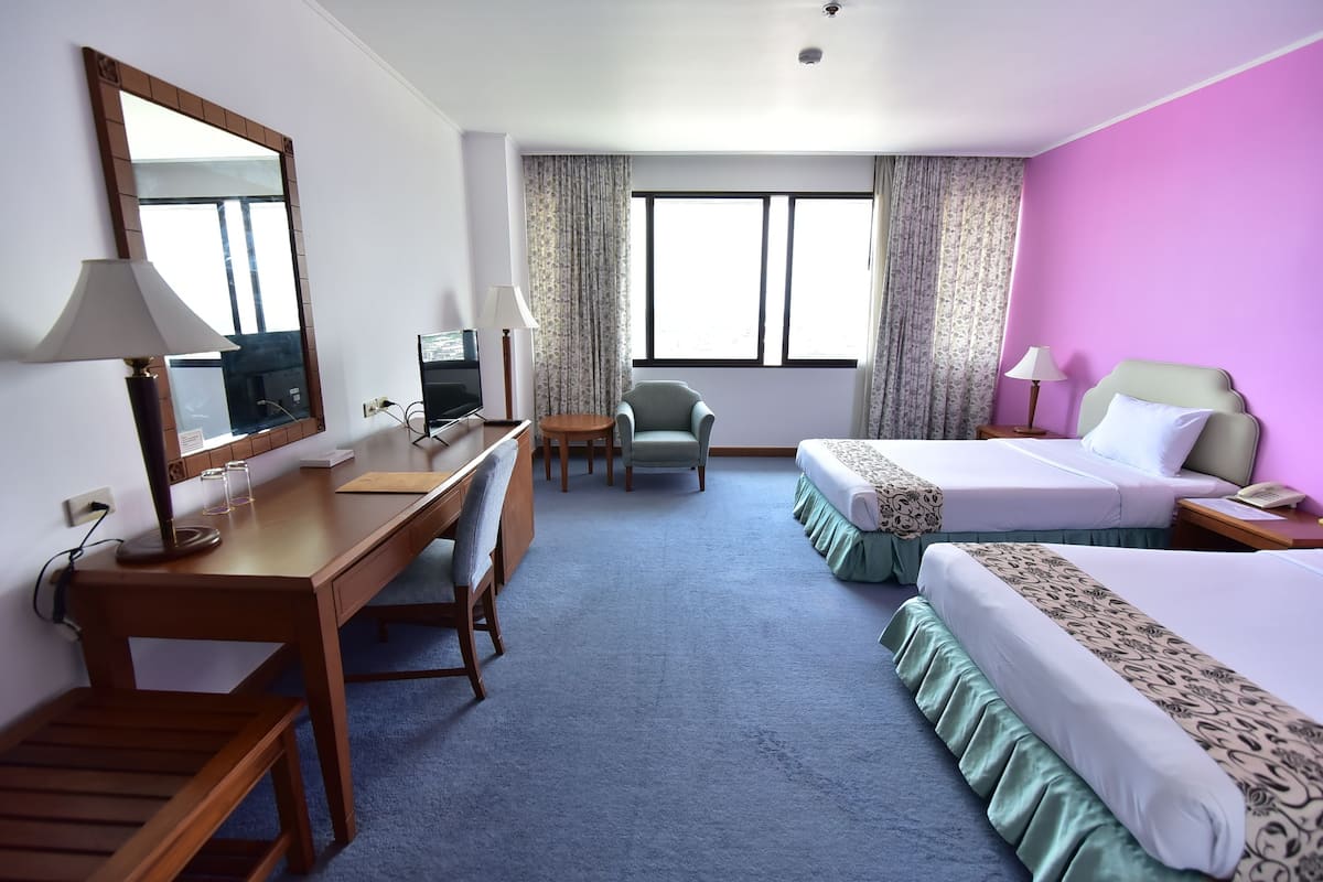 A hotel room with a desk, two beds, a chair, and a large window.