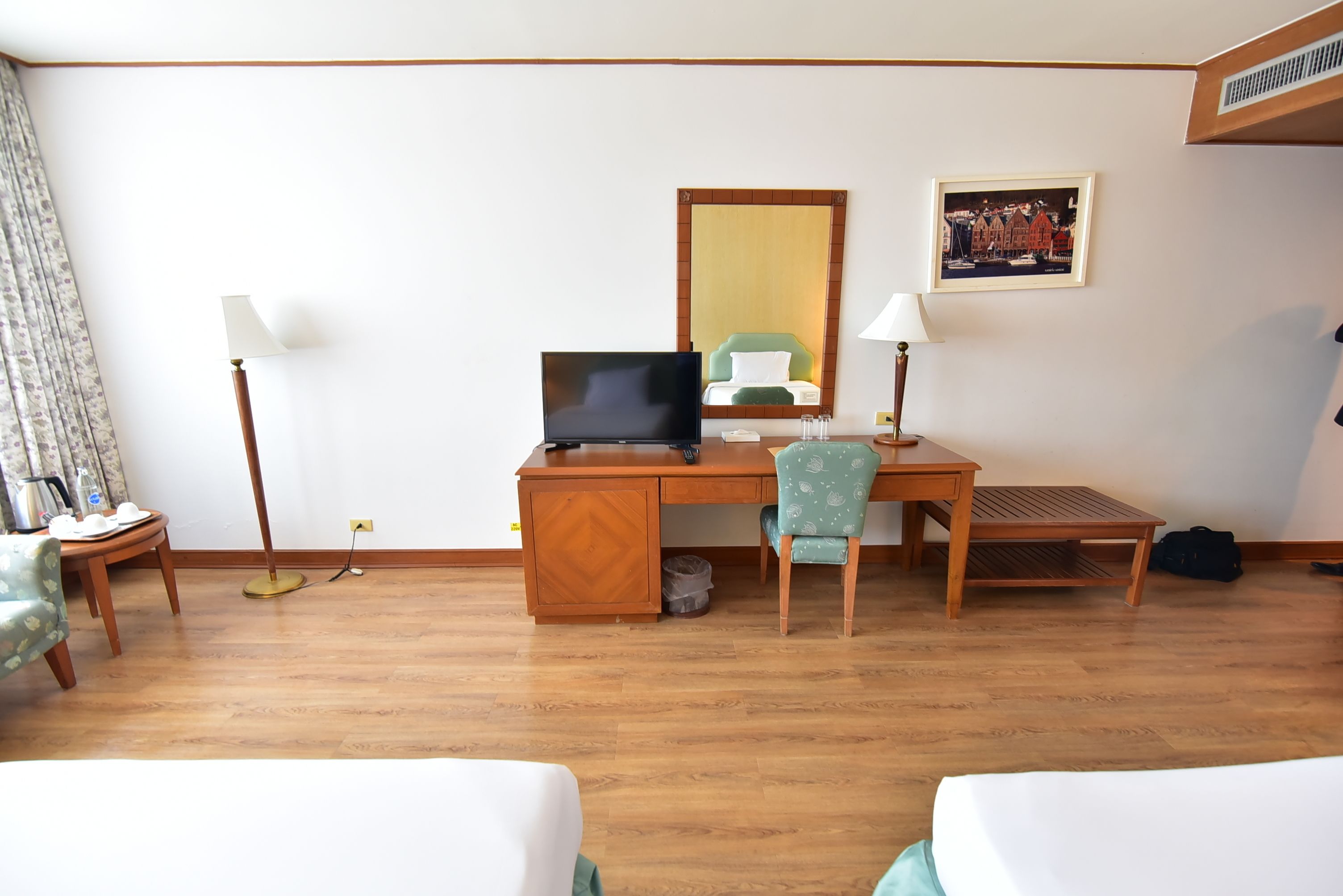 A hotel room with a wooden desk, a green chair, a bed, and a lamp.