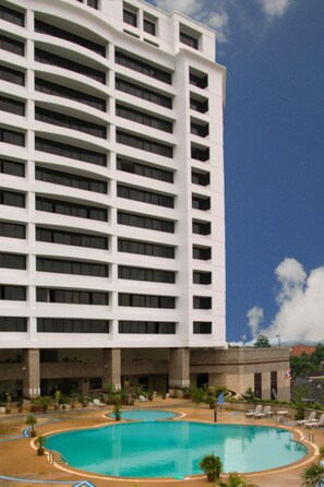 A multi-story hotel with a large pool area, including a central pool and a smaller pool with a curved design. - Thumrin Thana Hotel (Trang)