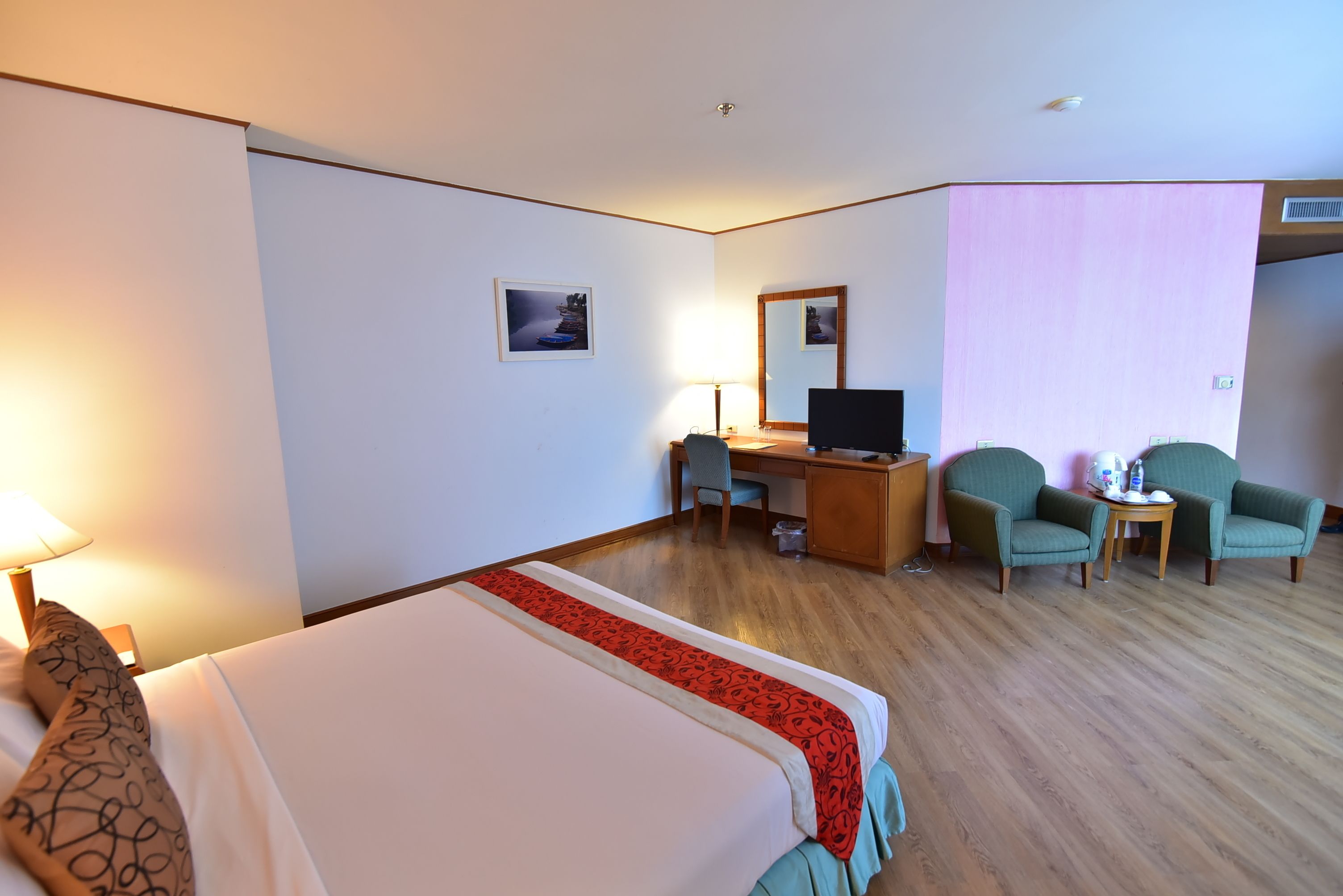 A hotel room with a large bed, a desk, two chairs, a TV, and a lamp.