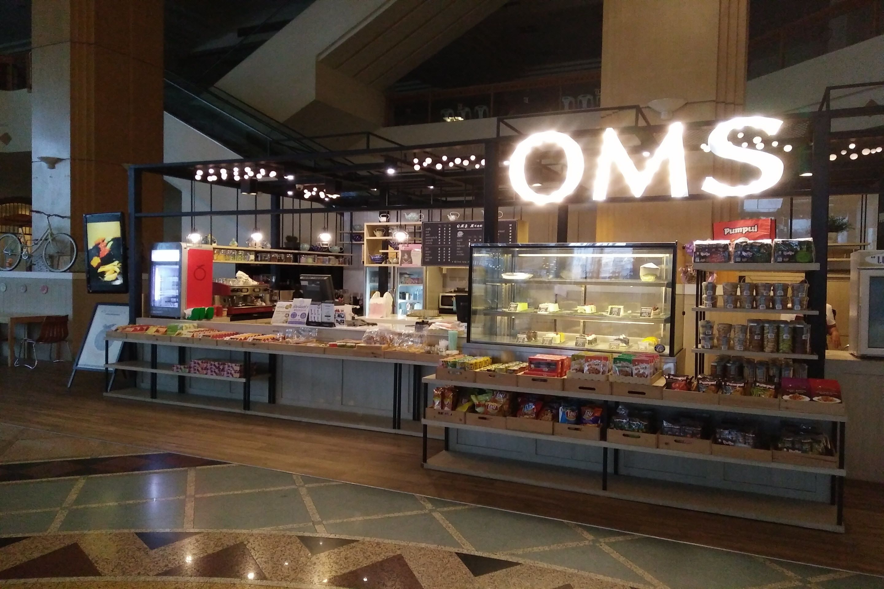 A food kiosk with a prominent 'OMS' sign, various food items displayed, and a refrigerated section.