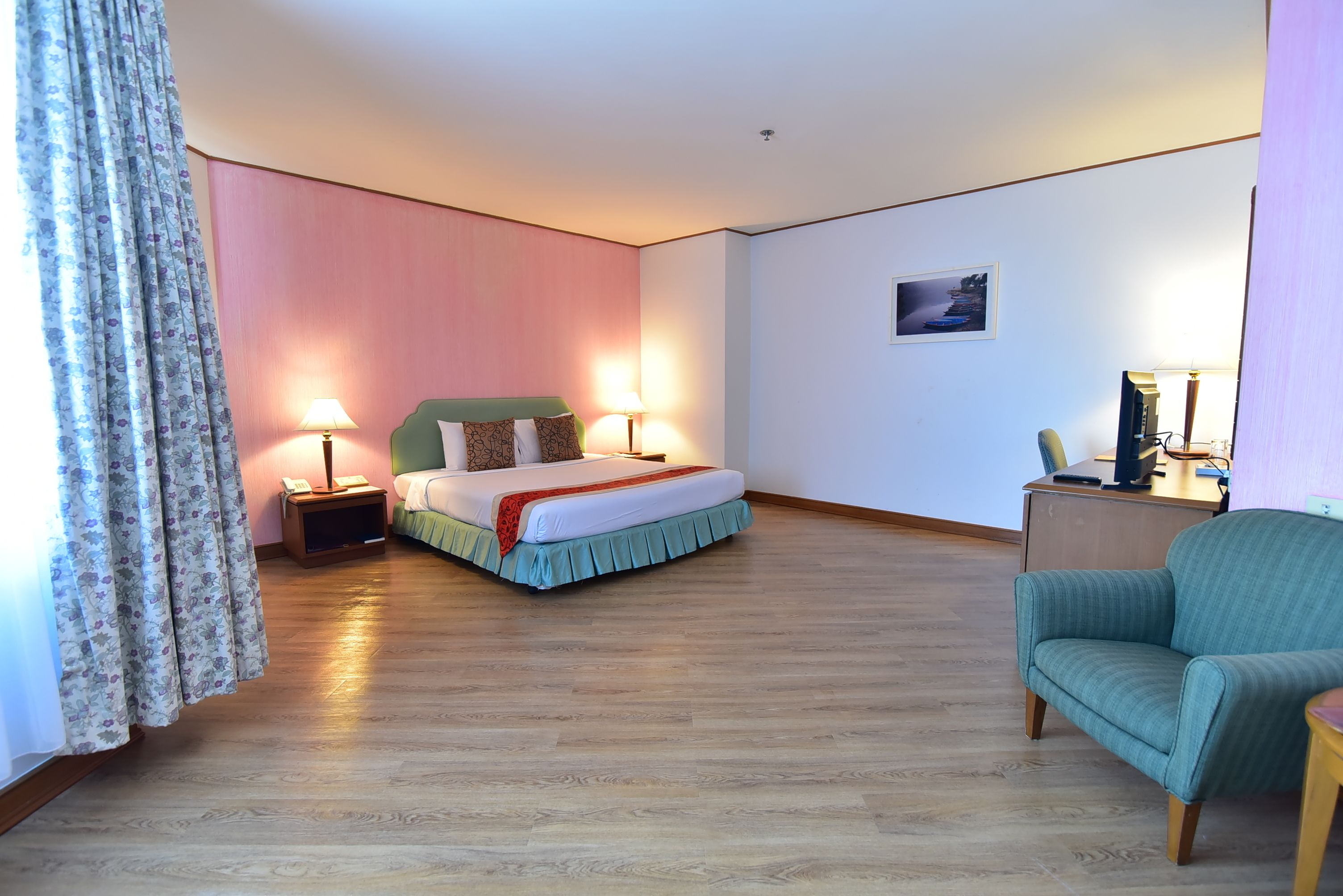 A hotel room with a bed, bedside lamps, a chair, a desk, and a picture on the wall.