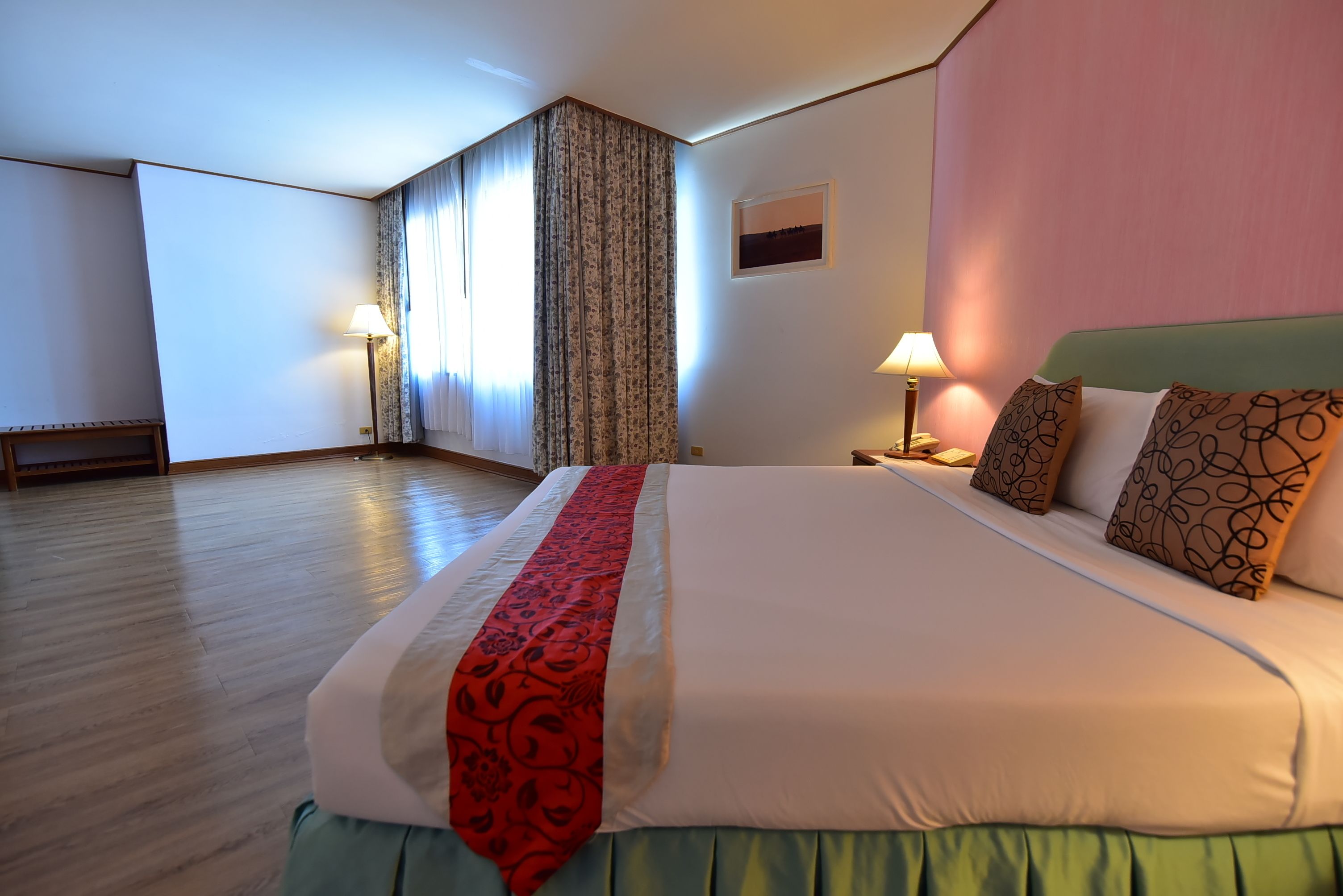 Een hotelkamer met een groot bed, twee bedlampjes, een raam met gordijnen en een houten vloer.