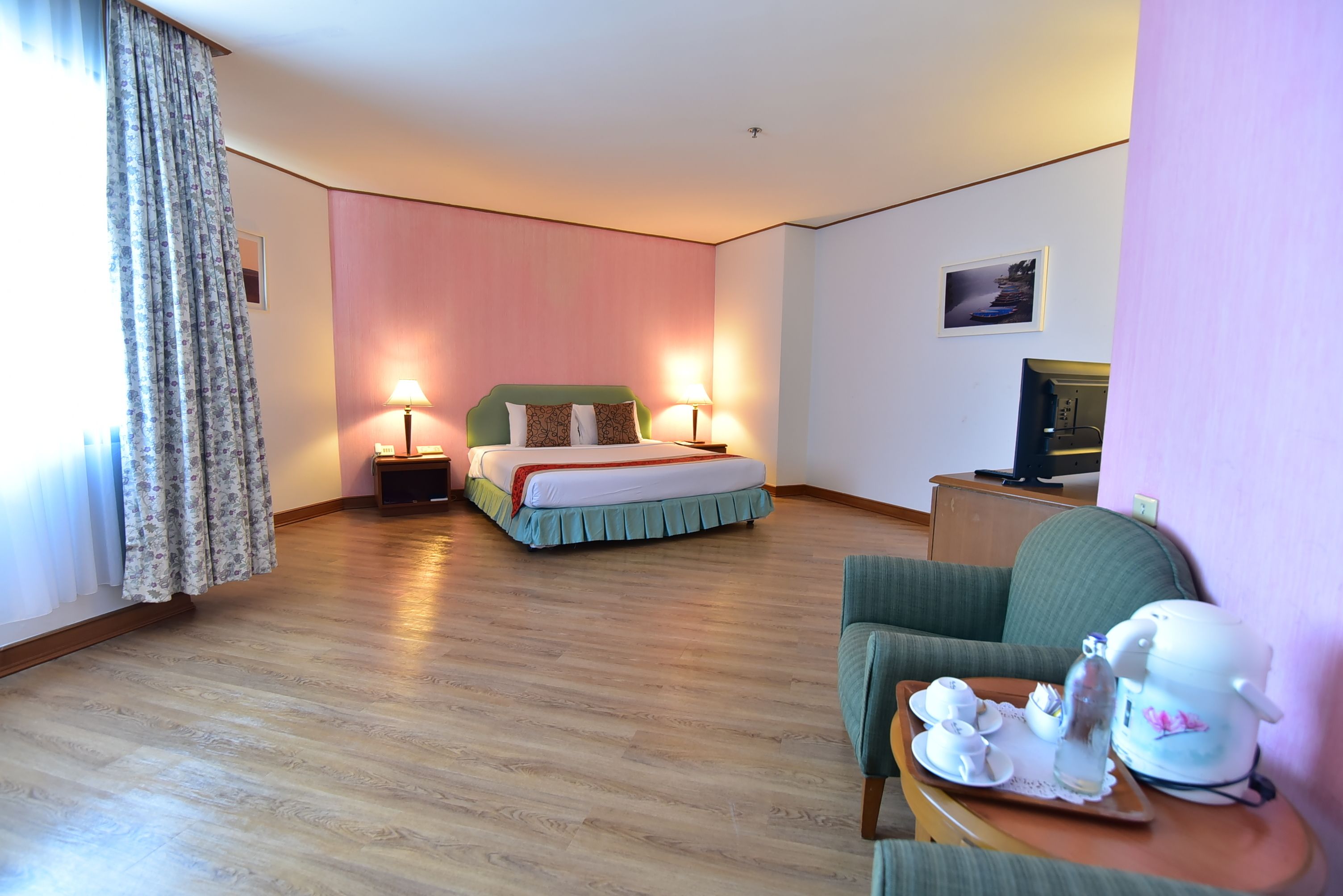 A hotel room with a bed, bedside lamps, a television, a sofa, and a tray with tea set.
