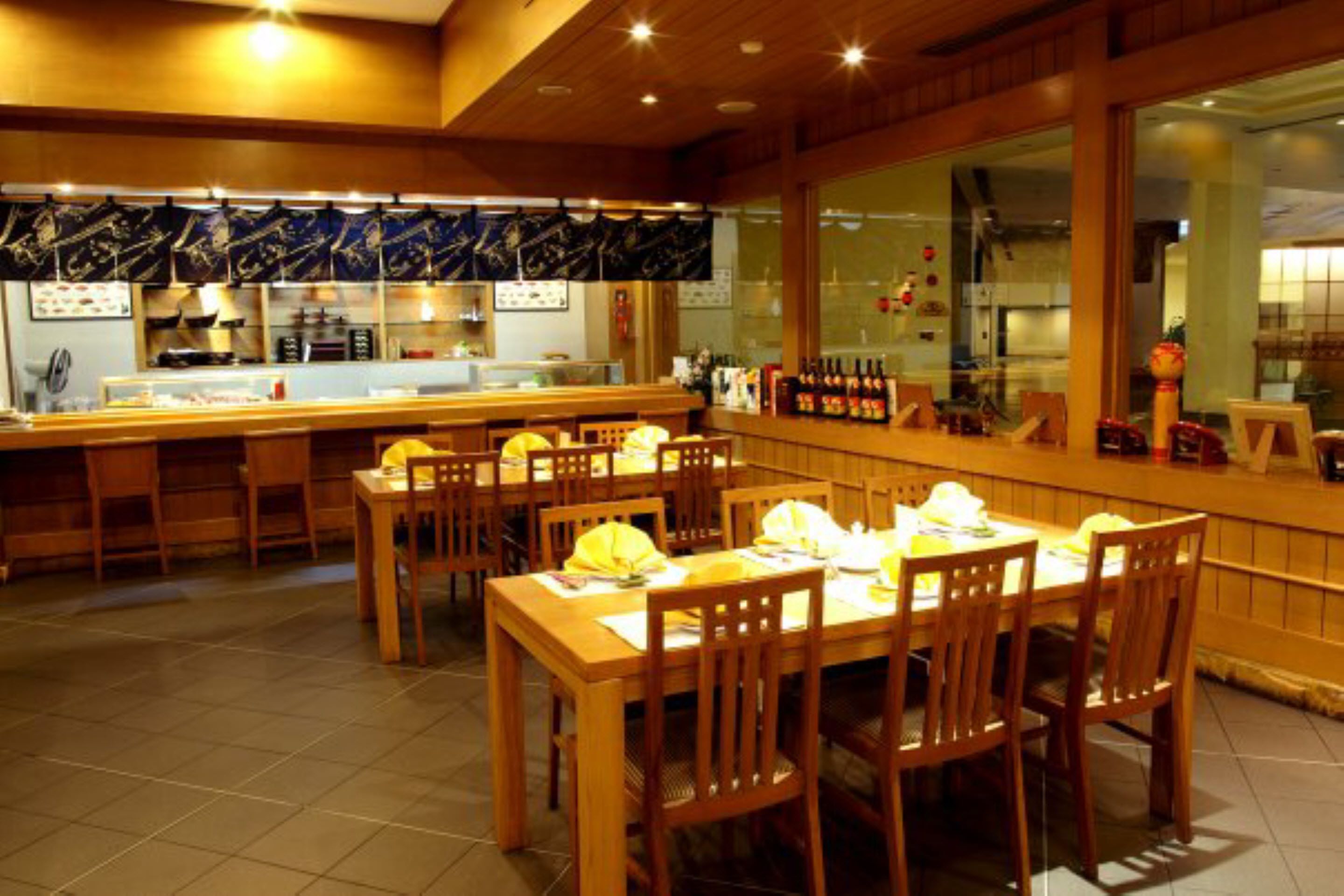 A restaurant with wooden tables and chairs, a counter with a display case, and a view through large windows.