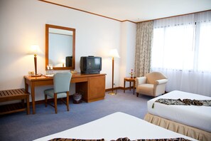 A hotel room with a bed, desk, chair, television, lamps, and a large window with curtains. - Thumrin Thana Hotel (Trang)