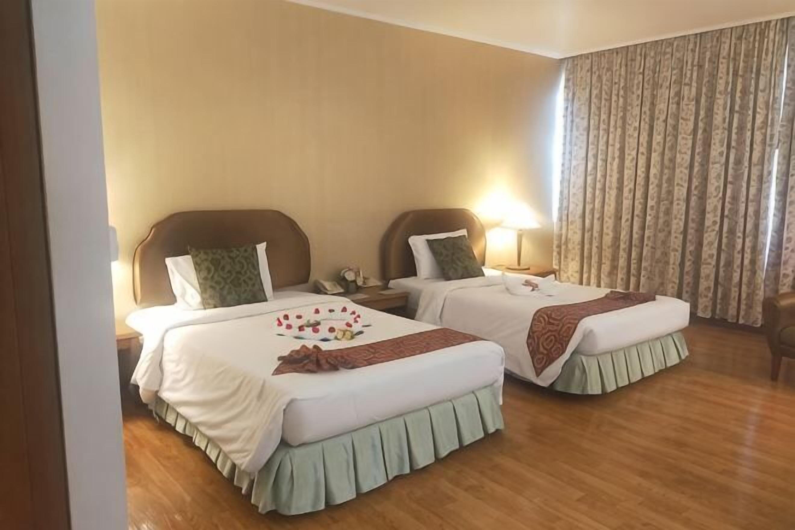 Una habitación de hotel con dos camas, suelo de madera y un amplio ventanal con cortinas.