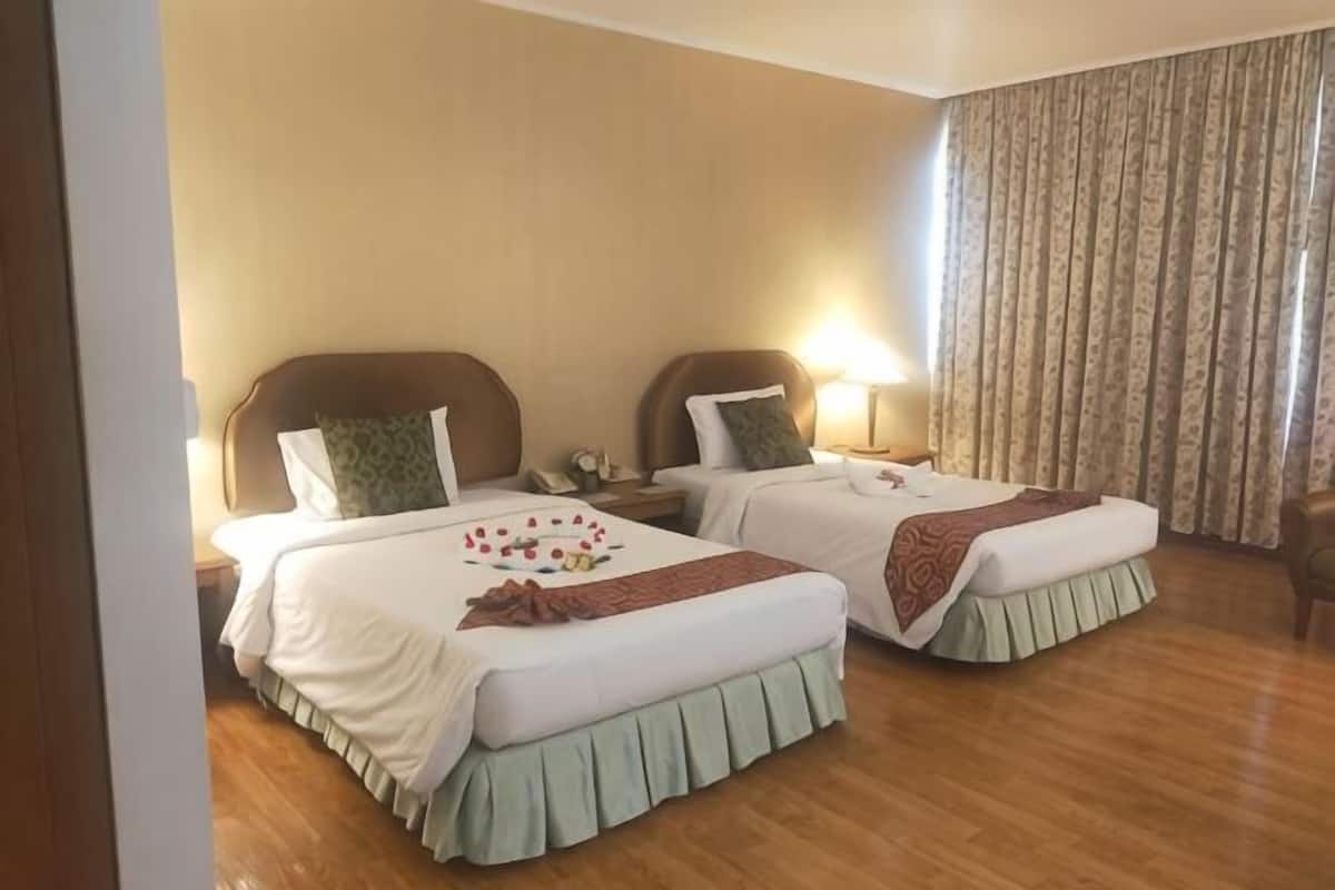 A hotel room with two beds, wooden flooring, and a large window with curtains.
