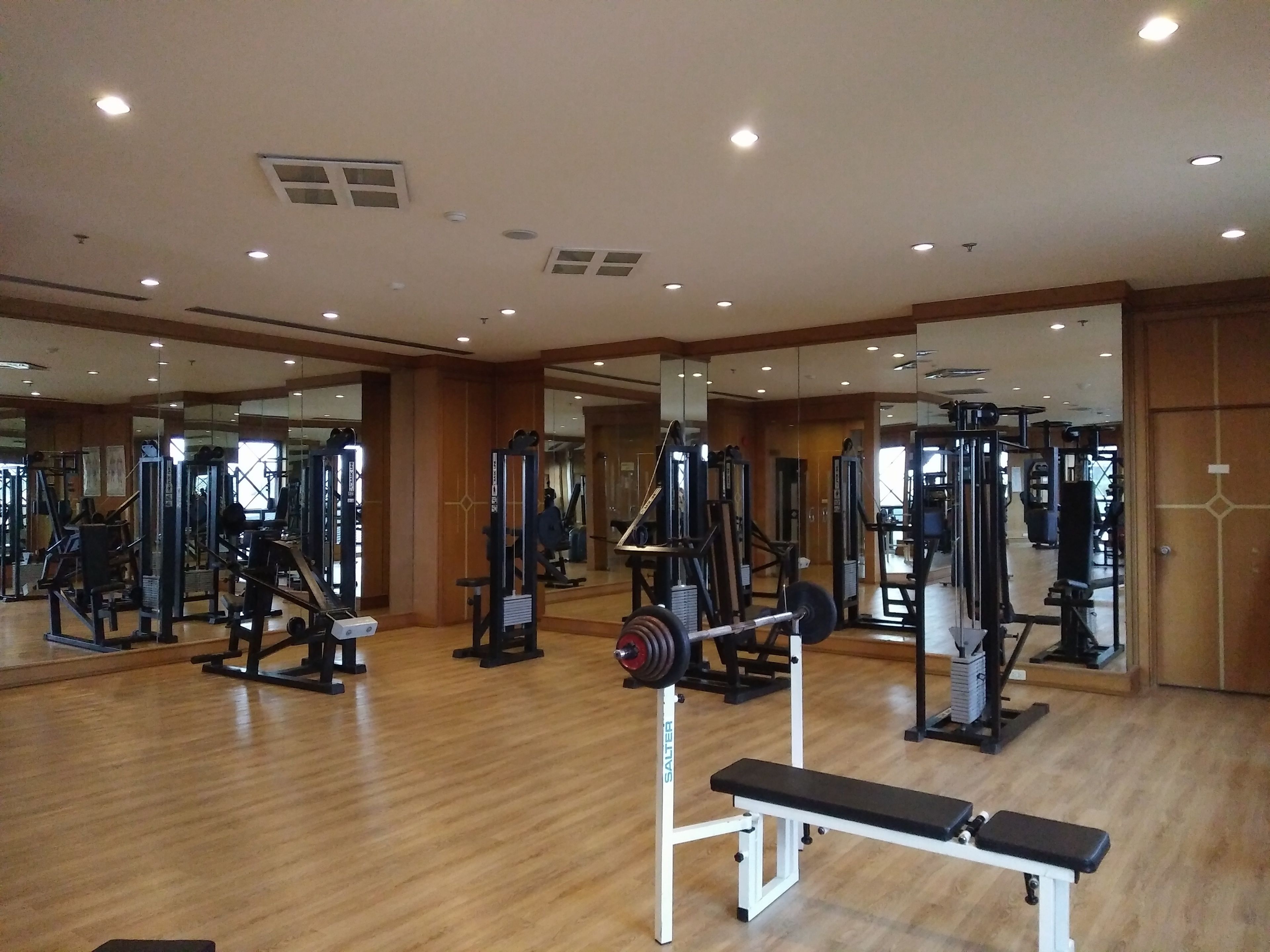 A gym with various exercise equipment, wooden floors, and mirrors on the walls.