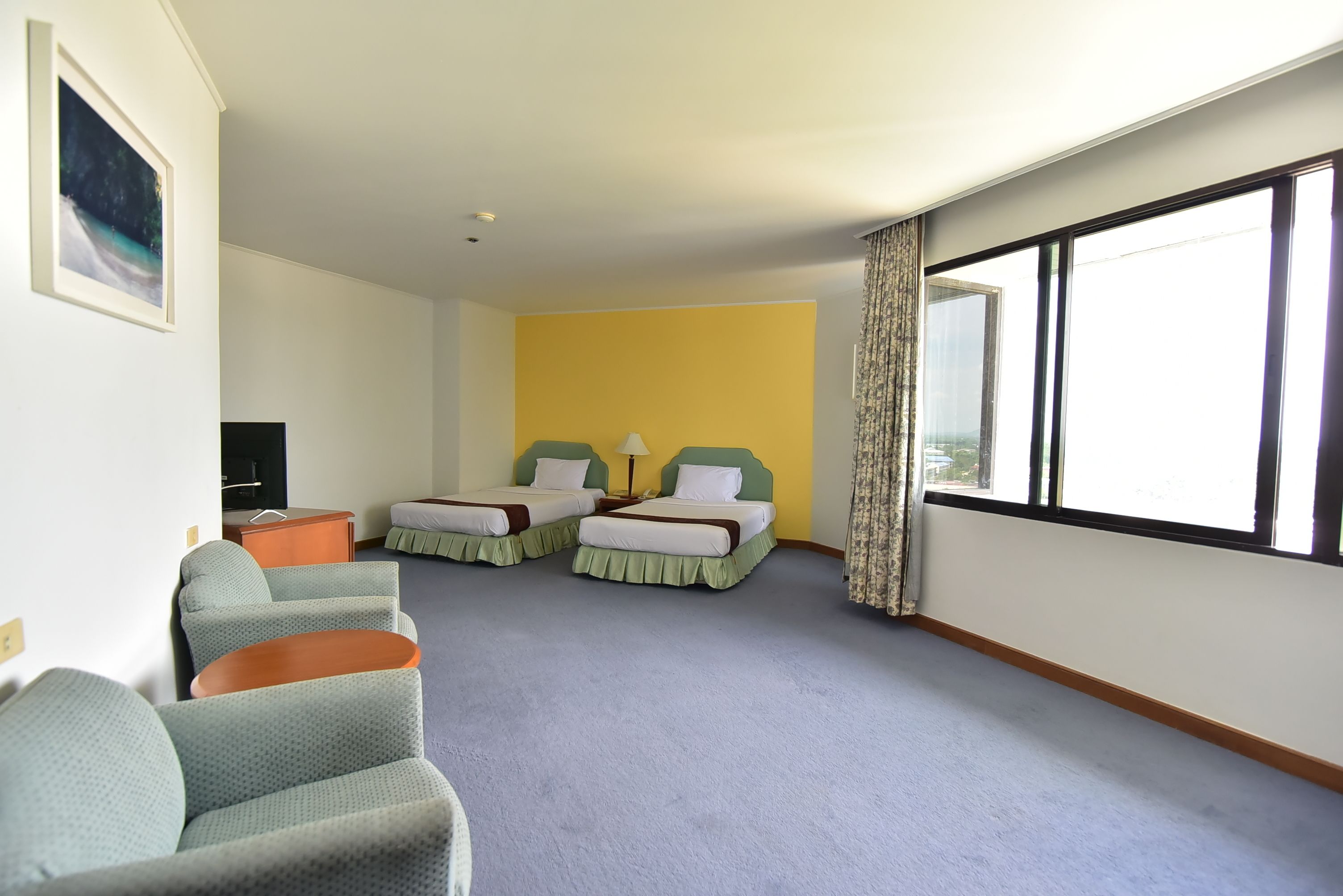A hotel room with two beds, a TV, a desk, and a large window.