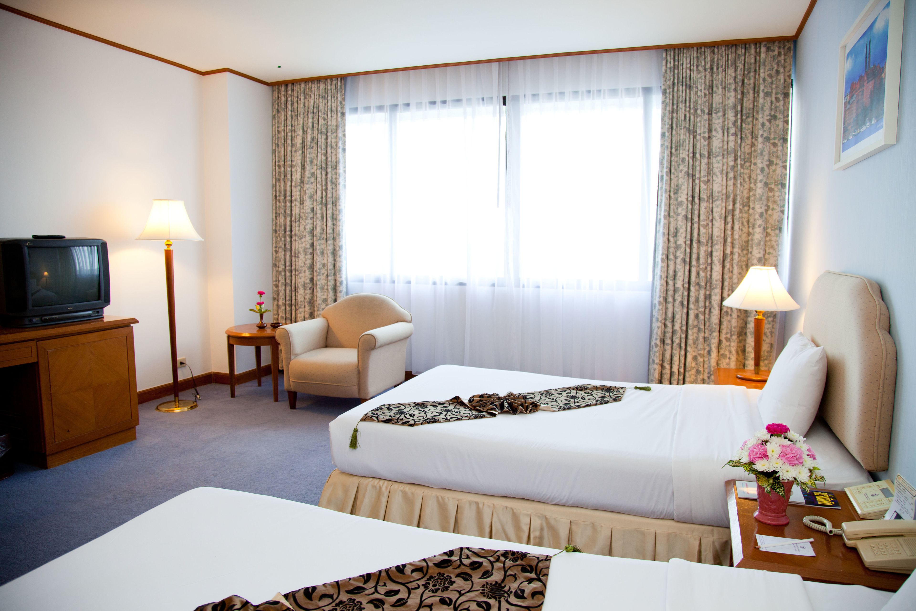 Una habitación de hotel con cama, una silla, escritorio con lámpara, teléfono y televisión.