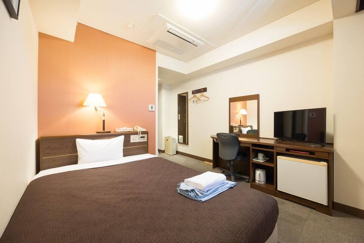 Una habitación de hotel con cama, escritorio, televisión y espejo.