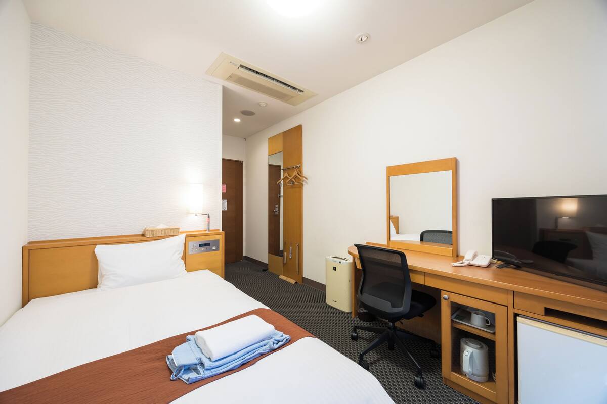 Habitación de hotel con cama, escritorio, silla, televisor y una kitchenette pequeña.