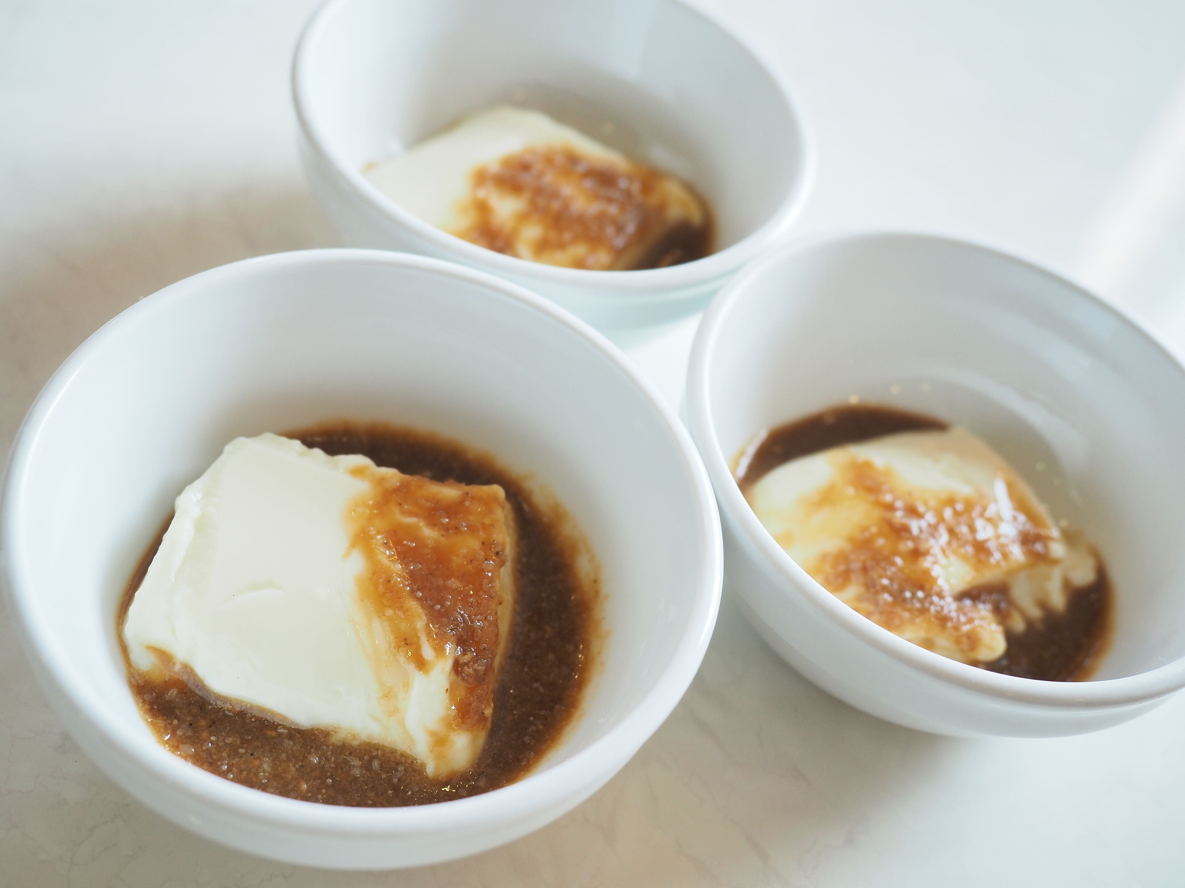 Three white bowls containing a dessert with caramelized top and a brown sauce.