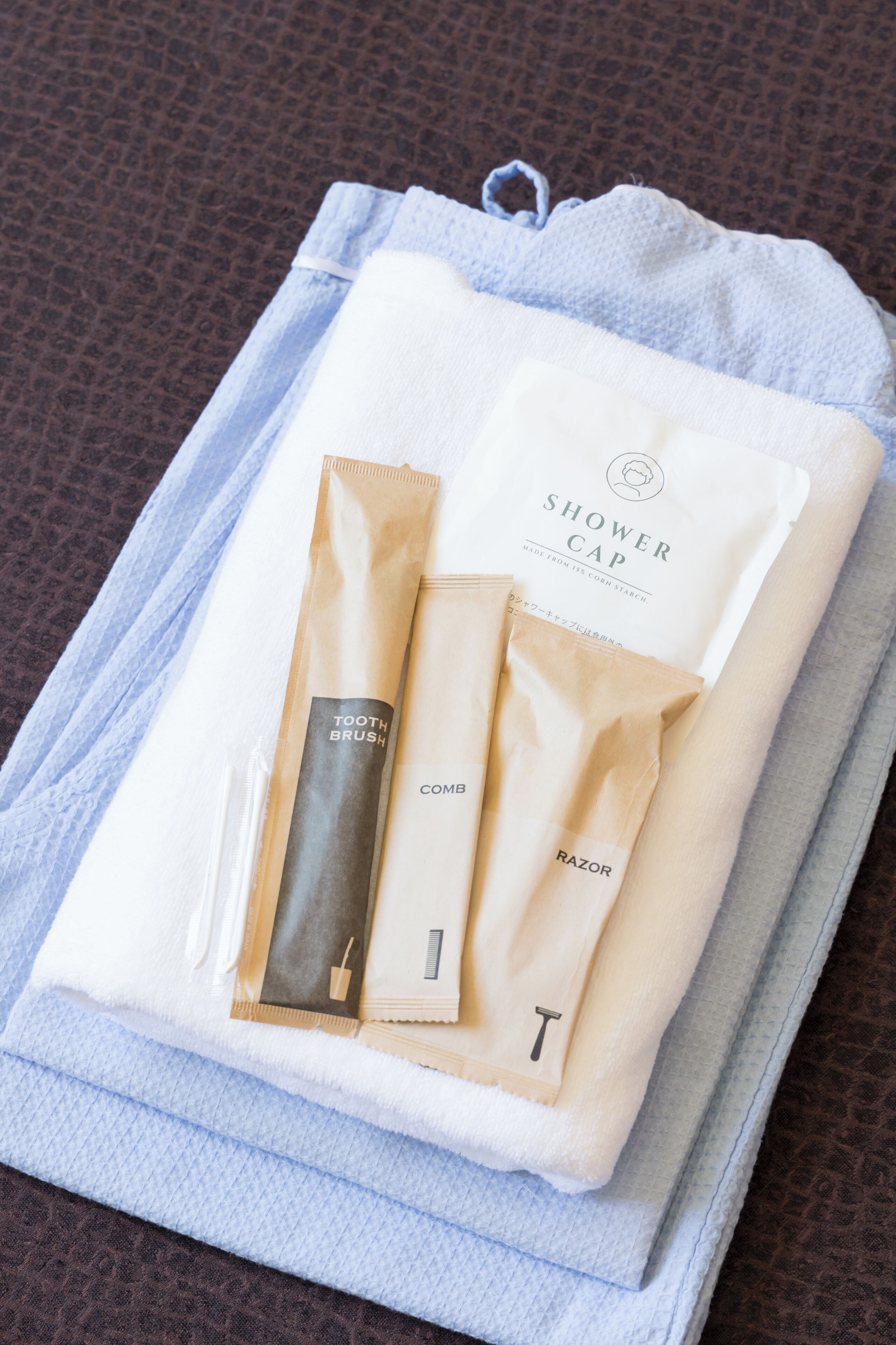 A neatly folded towel and a set of toiletries including a comb, razor, and toothbrush, placed on a textured brown surface.