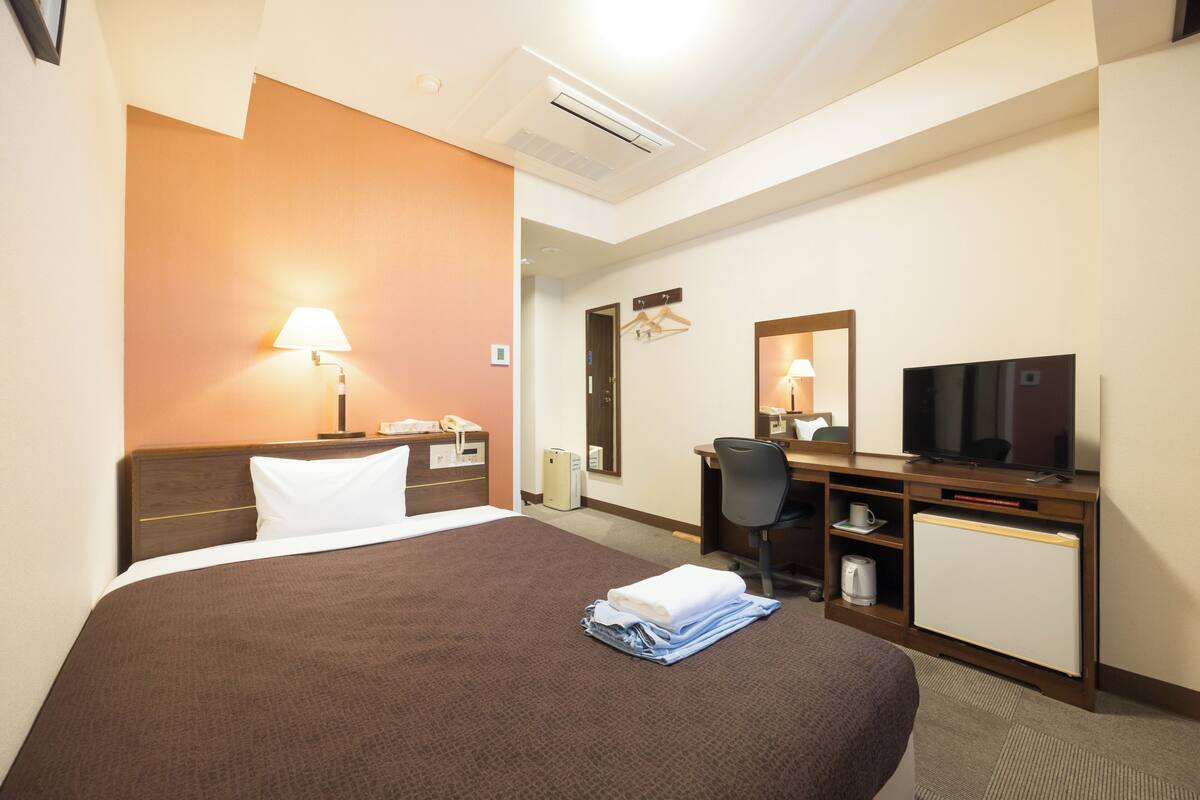 Una habitación de hotel con una cama grande, un escritorio con televisor, un espejo y un refrigerador pequeño.