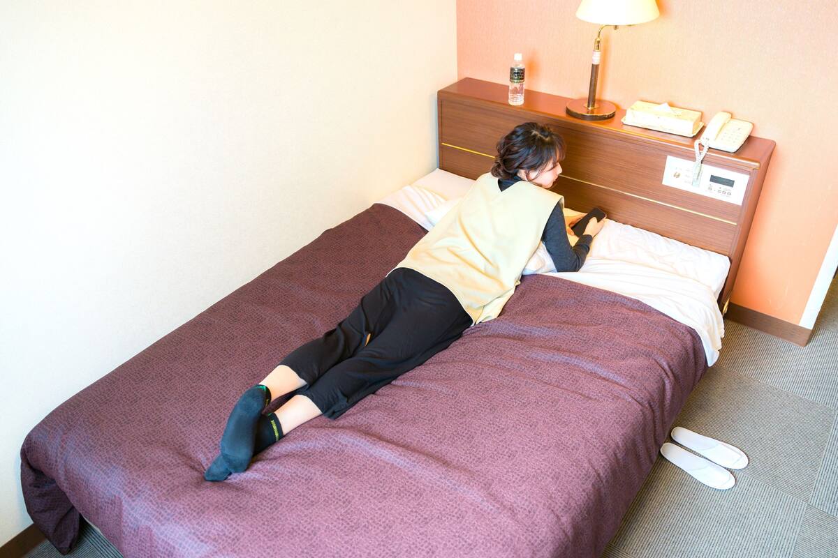 Una habitación de hotel con una cama, una mesita de noche con lámpara, un teléfono y una botella.