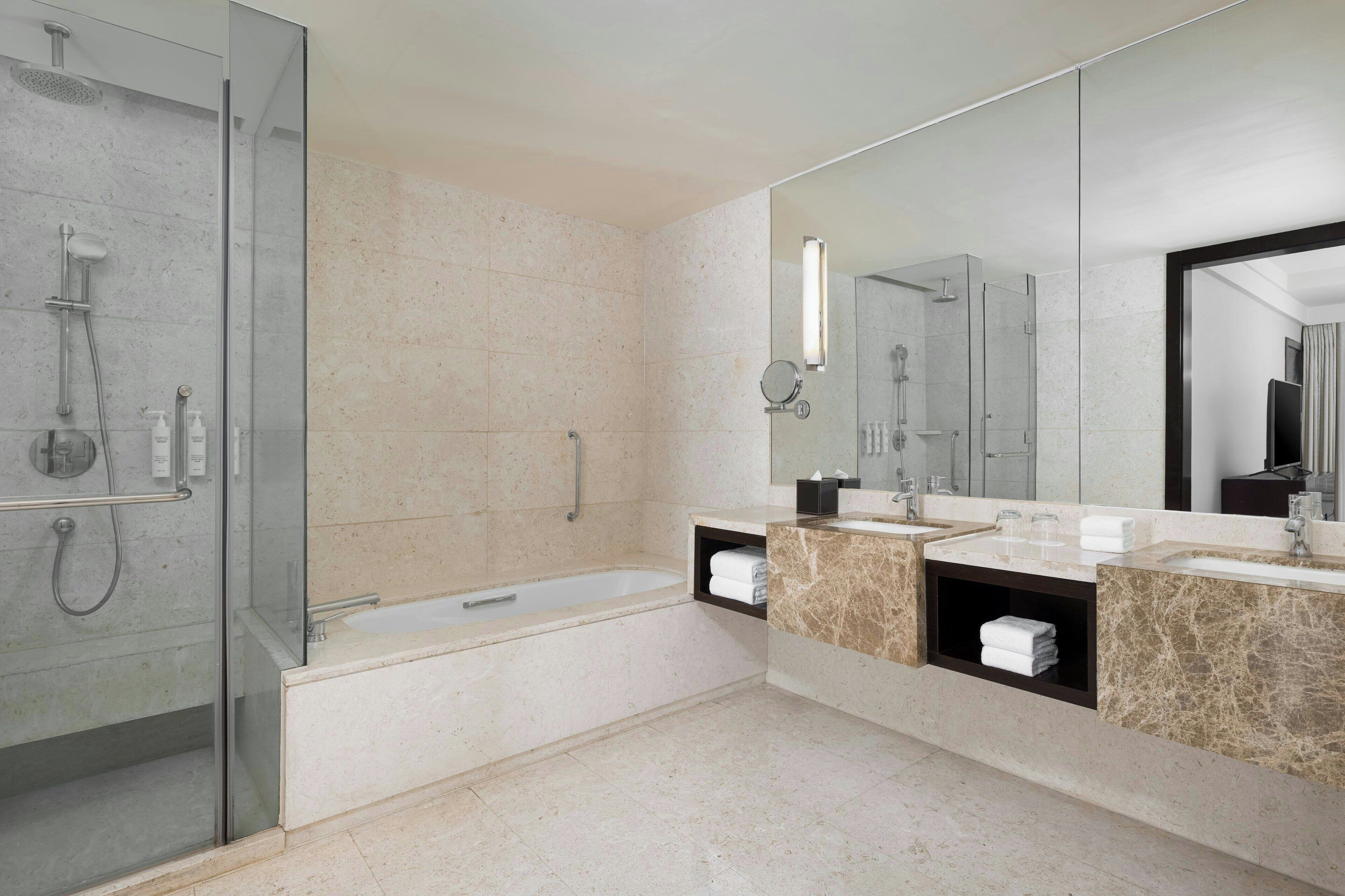 A modern bathroom with a glass-enclosed shower, a bathtub, and a vanity with two sinks and a mirror.