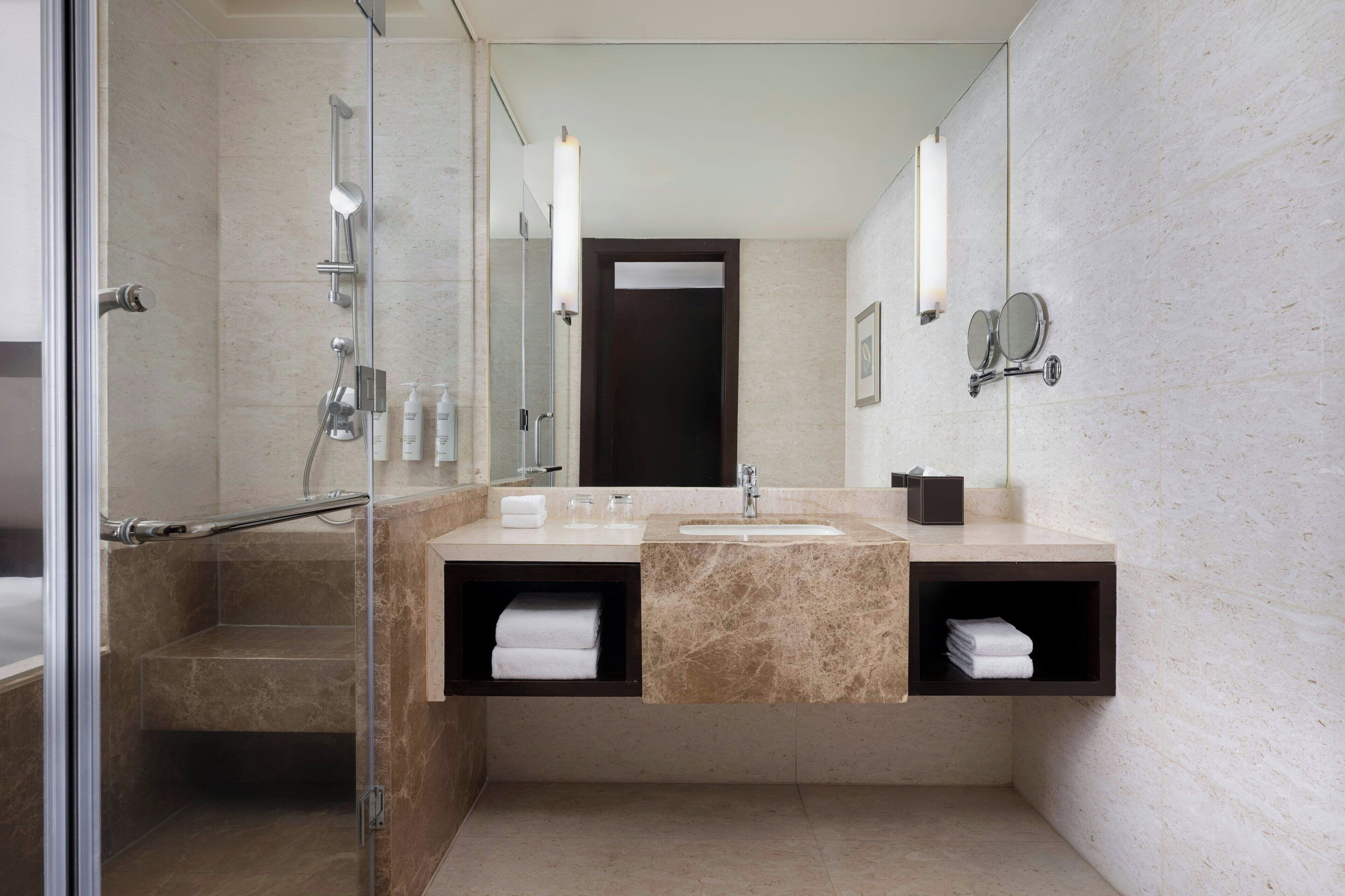 A modern bathroom with a glass-enclosed shower, a sink with a marble countertop, and two towel racks with folded towels.