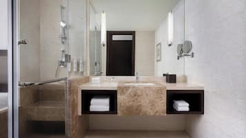 Ein modernes Badezimmer mit einer in Glas eingefassten Dusche, einem Waschbecken mit Marmorplatte und zwei Handtuchhaltern mit gefalteten Handtüchern.