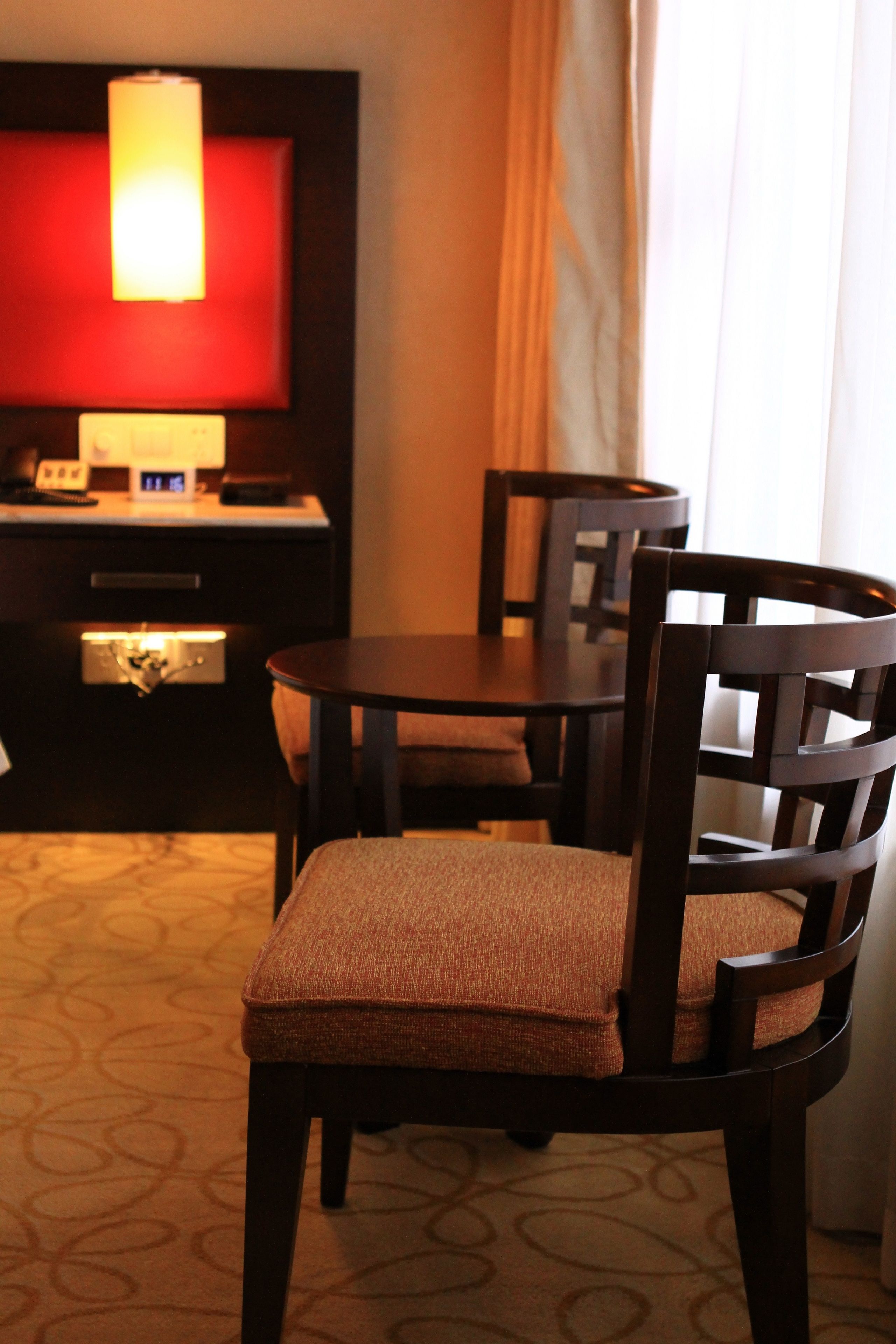 A hotel room with a dining table, two chairs, a television, and a lamp.