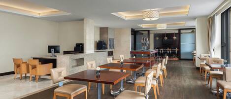 Un amplio vestíbulo de hotel con varias mesas y sillas para comer, una zona de recepción y un bar.