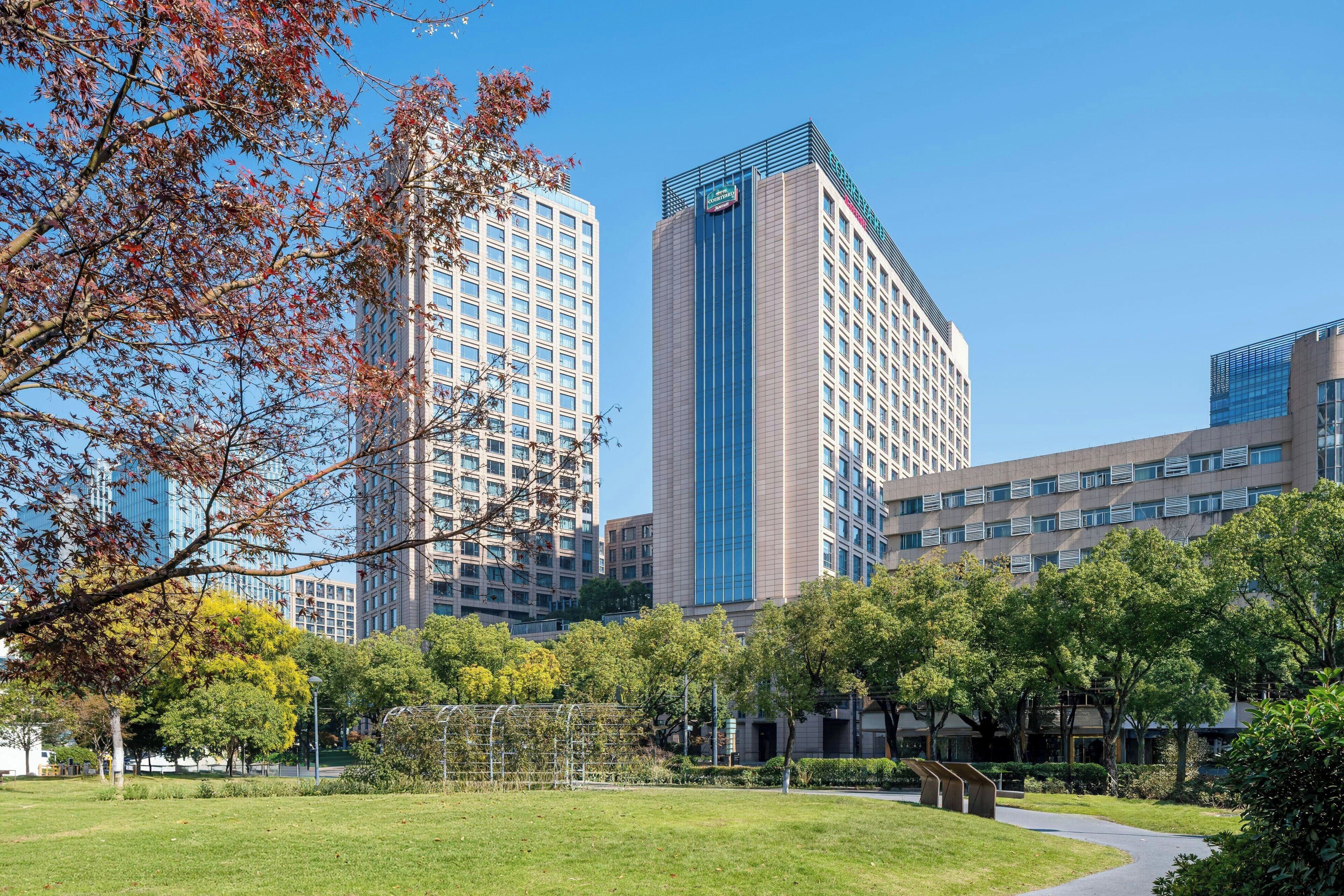 Un hotel moderno con una torre central, rodeado por un parque bien cuidado con senderos y árboles.