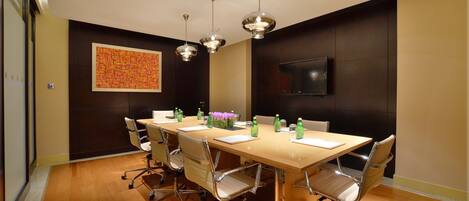 A conference room with a long table, six chairs, and three pendant lights.