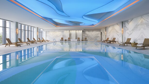Une piscine intérieure moderne, avec une eau d’un bleu limpide, des chaises longues disposées le long des bords et un plafond orné de motifs bleus évoquant des vagues.