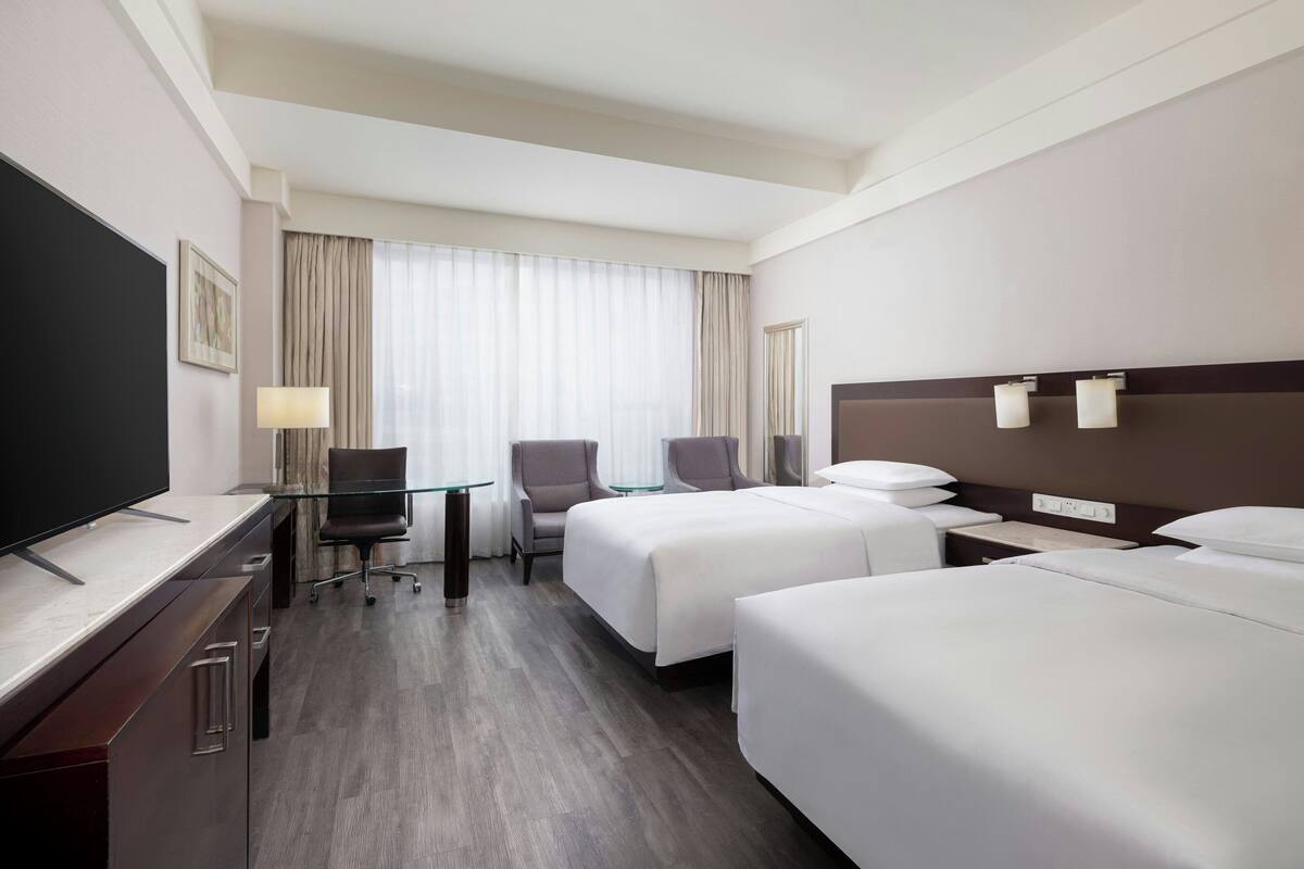 Une chambre d’hôtel avec deux lits, un bureau doté d’un téléviseur à écran plat, une chaise et une lampe.