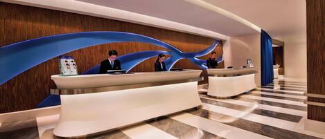 A modern hotel reception area with a curved reception desk, a wooden wall with a blue wave design, and a check-in counter.