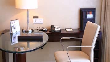 Una habitación de hotel con escritorio, silla, lámpara, teléfono y un cuadro en la pared.