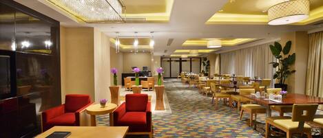 A hotel lobby with a long reception desk, multiple seating areas, and a patterned carpet.