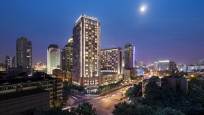 Un hôtel JW Marriott au design moderne, entouré d’autres immeubles de grande hauteur et bordant une rue animée de la ville, au crépuscule.