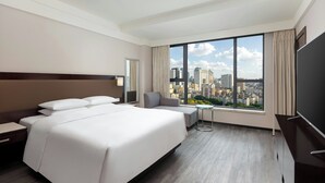 Une chambre d’hôtel avec un grand lit, un petit coin salon, une télévision et une vue sur la ville.